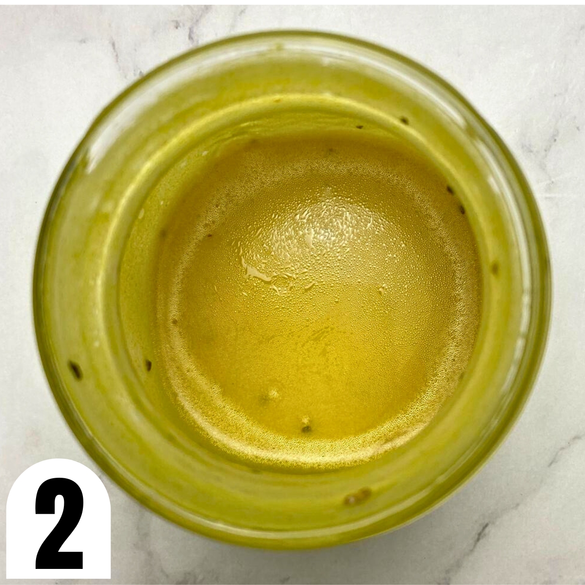 Glass jar with a mustard, black pepper and oil dressing in it.